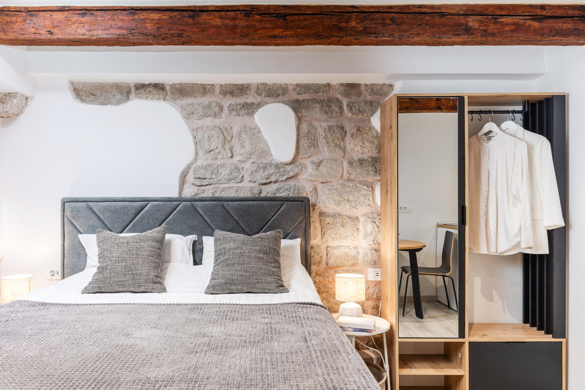 The bedroom — original limestone wall, chestnut beams, queen bed with grey linen